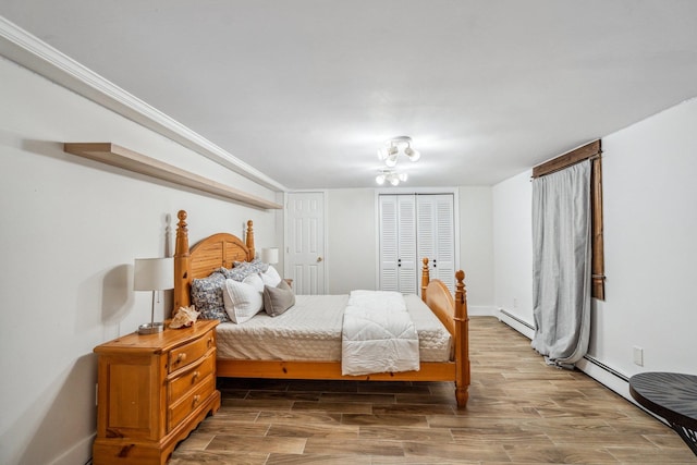 bedroom featuring a baseboard heating unit, baseboards, wood finished floors, and a closet