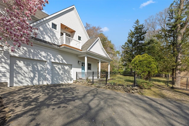 view of property exterior with covered porch, driveway, a balcony, and fence