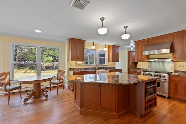 kitchen featuring a sink, visible vents, wall chimney range hood, a kitchen island, and appliances with stainless steel finishes