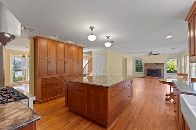 kitchen featuring wall chimney exhaust hood, light wood-style flooring, visible vents, a ceiling fan, and a fireplace