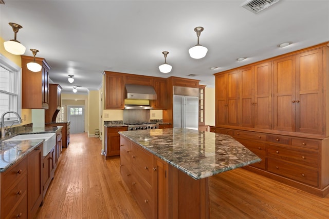 kitchen with stainless steel appliances, visible vents, wall chimney range hood, a sink, and light wood-style flooring
