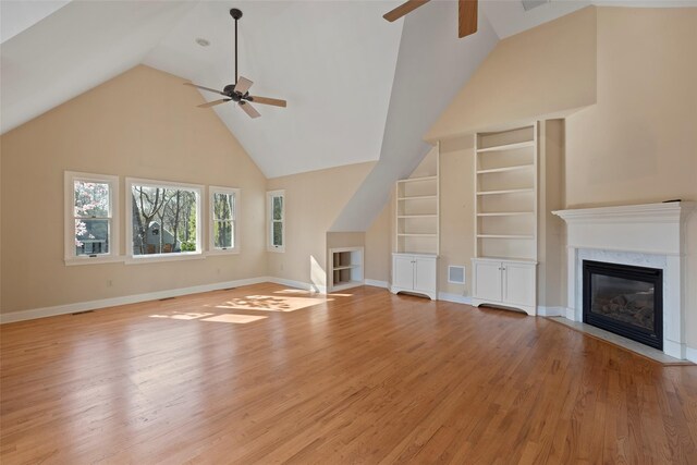 unfurnished living room with visible vents, light wood-style floors, built in shelves, a ceiling fan, and a fireplace