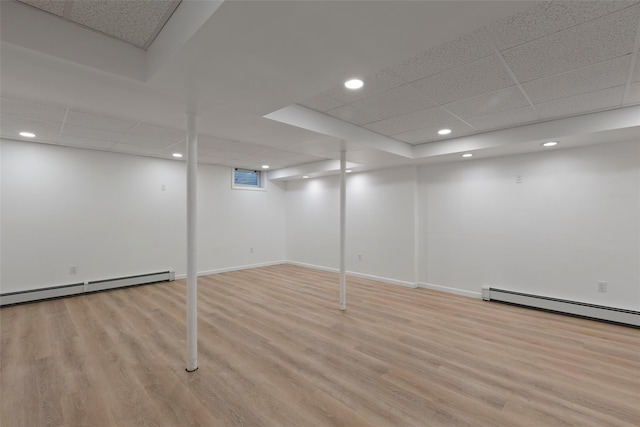 finished basement with a baseboard heating unit, light wood finished floors, baseboards, a paneled ceiling, and recessed lighting