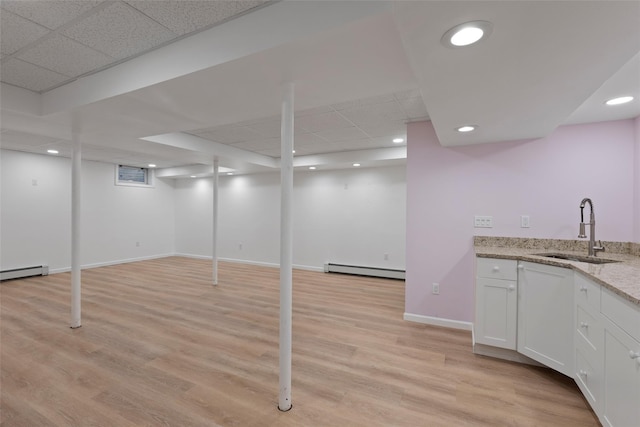 finished below grade area with recessed lighting, a drop ceiling, a sink, light wood-style floors, and baseboard heating