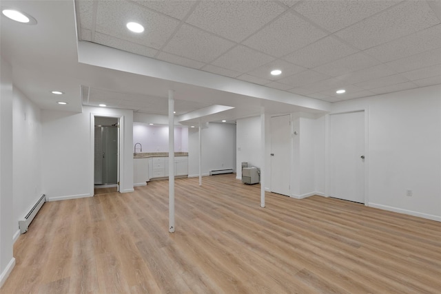 finished below grade area with a baseboard radiator, light wood-style flooring, baseboards, and a baseboard heating unit