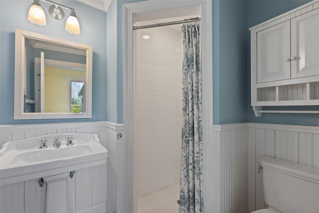 bathroom with toilet, tiled shower, a sink, and wainscoting