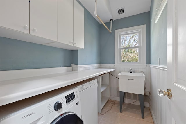 clothes washing area with wainscoting, visible vents, washer / clothes dryer, cabinet space, and light tile patterned floors
