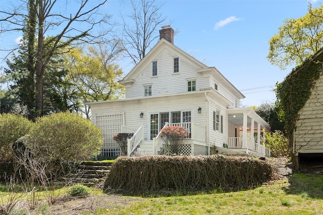 rear view of property with stairway, covered porch, and a chimney