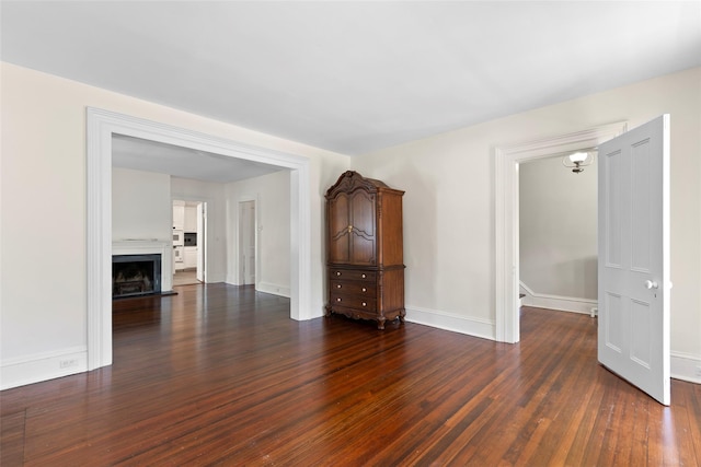 unfurnished living room with a fireplace, dark wood-style floors, and baseboards