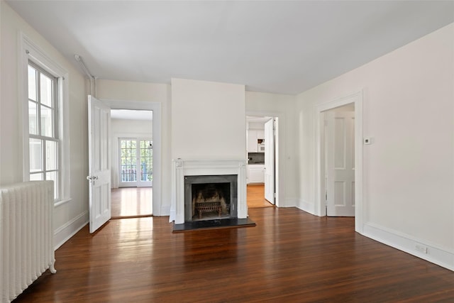 unfurnished living room with baseboards, radiator heating unit, wood finished floors, and a fireplace with raised hearth
