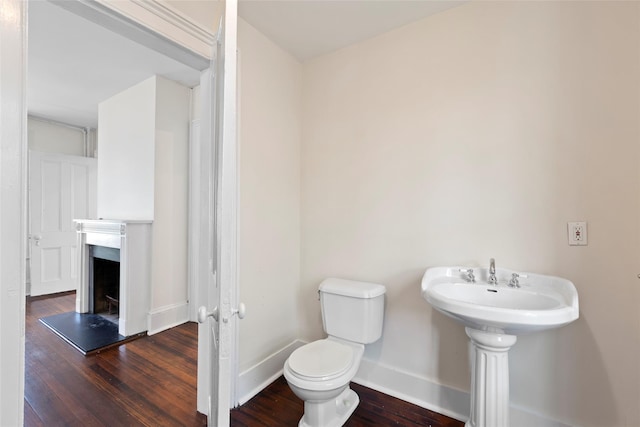 bathroom featuring a fireplace, wood finished floors, toilet, and baseboards