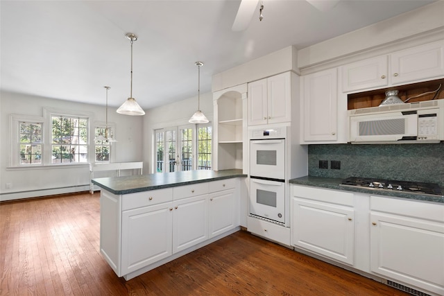 kitchen featuring dark countertops, a peninsula, open shelves, and white appliances