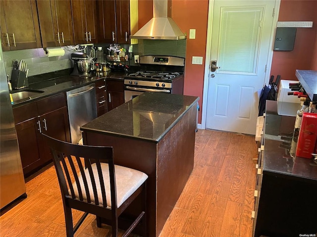 19 Tatterson St, Roslyn, NY 11576 - kitchen featuring dark stone counters, light wood-type flooring, dark brown cabinetry, wall chimney exhaust hood, and appliances with stainless steel finishes