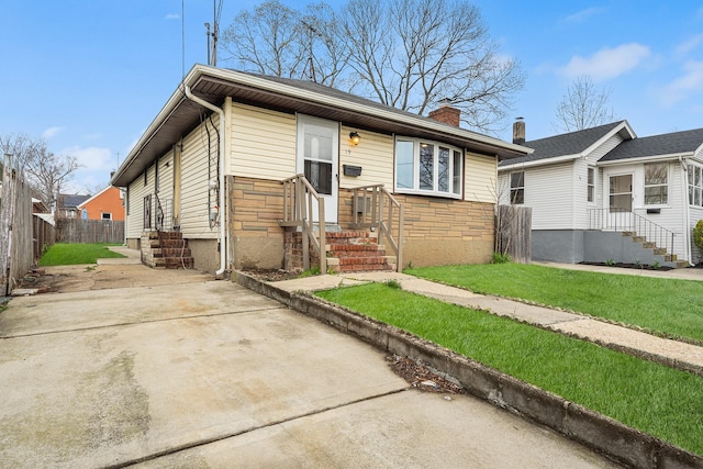 view of front of home with driveway, entry steps, a chimney, fence, and a front lawn
