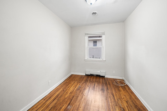 empty room featuring visible vents, hardwood / wood-style floors, a baseboard heating unit, and baseboards