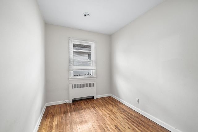 spare room with radiator heating unit, visible vents, baseboards, and wood-type flooring