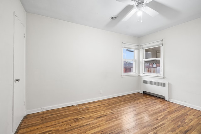 spare room featuring hardwood / wood-style flooring, radiator, baseboards, visible vents, and a ceiling fan