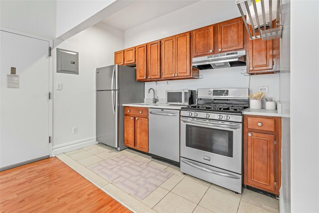kitchen with appliances with stainless steel finishes, under cabinet range hood, light countertops, and a sink
