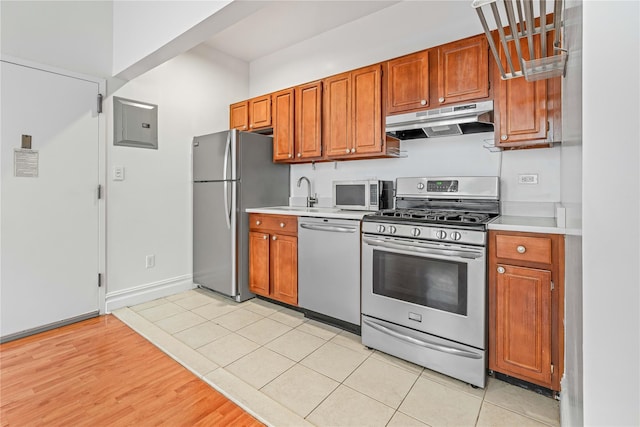 kitchen with stainless steel appliances, under cabinet range hood, light countertops, and a sink