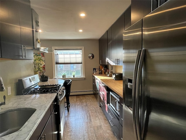 kitchen featuring wood finished floors, a sink, a baseboard radiator, stainless steel appliances, and butcher block countertops