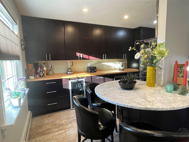 kitchen with dark cabinets, a breakfast bar, baseboard heating, and light wood-style flooring