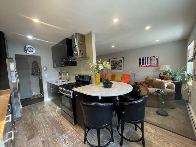 kitchen with wall chimney range hood, a sink, gas stove, light countertops, and light wood-type flooring