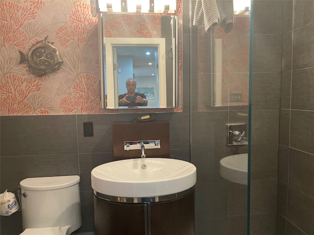 bathroom featuring a sink, tile walls, wallpapered walls, and toilet