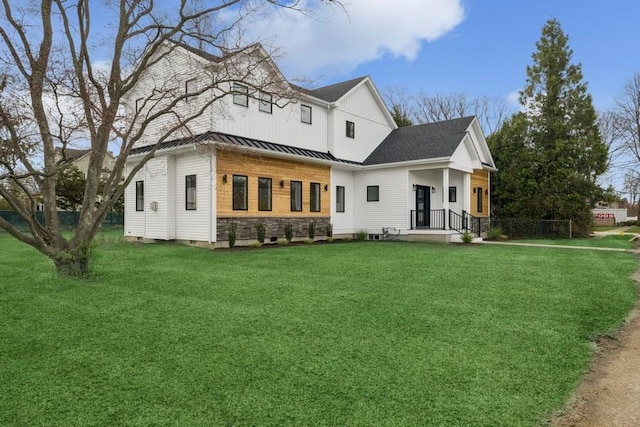 back of house featuring a standing seam roof, a lawn, stone siding, and metal roof