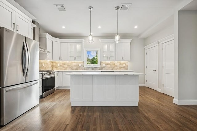 kitchen with appliances with stainless steel finishes, decorative backsplash, light countertops, wall chimney range hood, and a center island