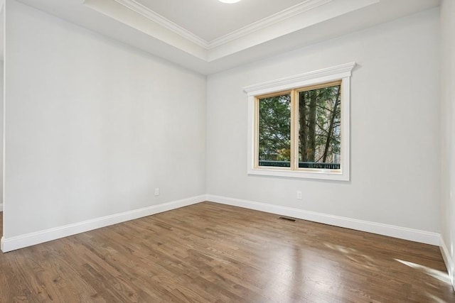 empty room with crown molding, baseboards, wood finished floors, and a raised ceiling