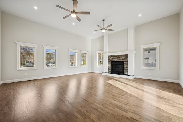 unfurnished living room with ceiling fan, wood finished floors, a stone fireplace, recessed lighting, and baseboards