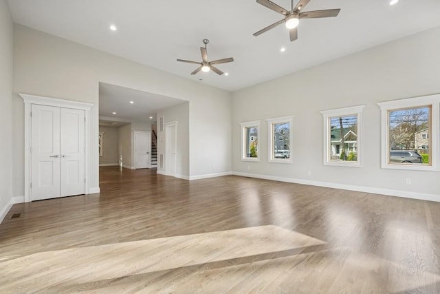unfurnished living room with plenty of natural light, a ceiling fan, wood finished floors, recessed lighting, and baseboards