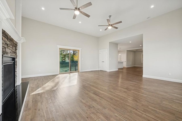 unfurnished living room with ceiling fan, a fireplace, wood finished floors, recessed lighting, and baseboards