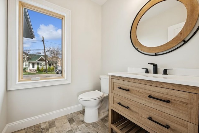 half bath featuring baseboards, toilet, vanity, and stone finish flooring