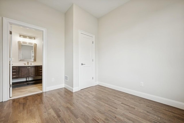 unfurnished bedroom with wood finished floors, a sink, baseboards, and connected bathroom