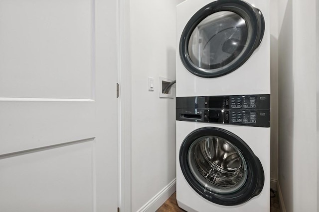 clothes washing area with stacked washer / dryer, baseboards, and wood finished floors