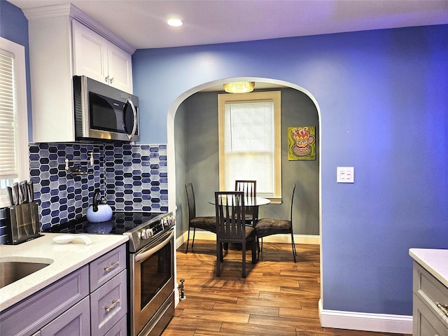 132-29 Brookville Blvd, Rosedale, NY 11422 - kitchen featuring stainless steel appliances, wood finished floors, backsplash, baseboards, and arched walkways