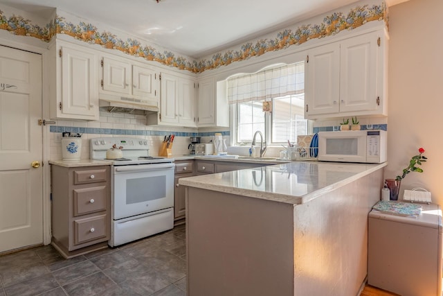 kitchen featuring white appliances, under cabinet range hood, a sink, white cabinets, and a peninsula