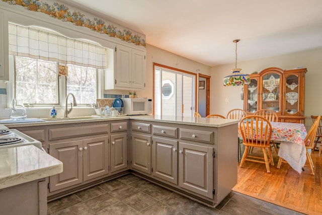 kitchen with a sink, a peninsula, white microwave, backsplash, and white cabinets