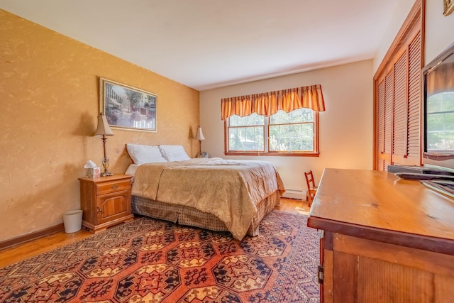 bedroom with a baseboard heating unit, wood finished floors, multiple windows, baseboards, and a textured wall