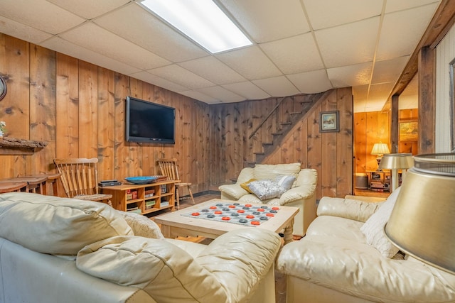 living room with a paneled ceiling, wood walls, and stairway