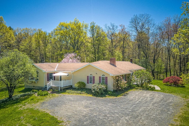 view of front of home with a porch, gravel driveway, and a chimney