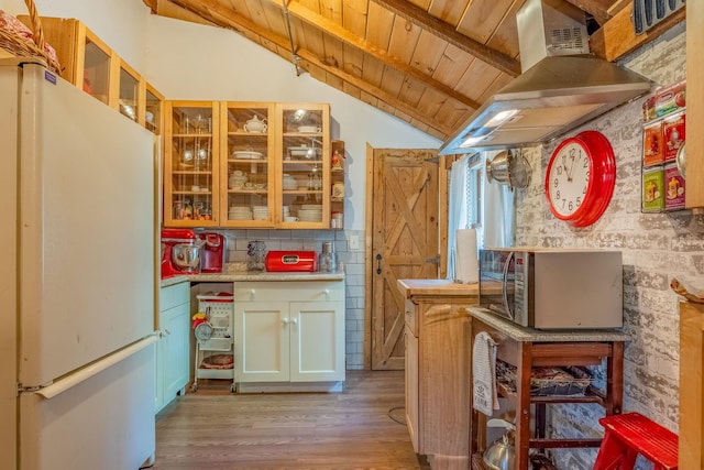 kitchen featuring freestanding refrigerator, exhaust hood, stainless steel microwave, wood ceiling, and light wood-style flooring