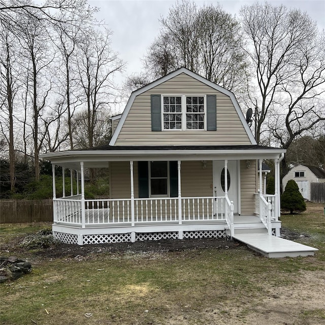 view of front of home featuring a gambrel roof, a front yard, covered porch, and fence