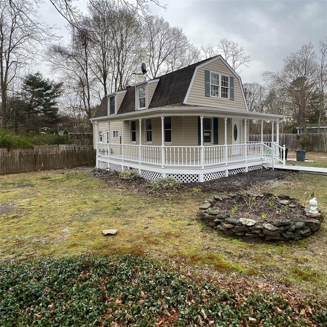 view of front of house featuring a gambrel roof, a porch, a front yard, and fence