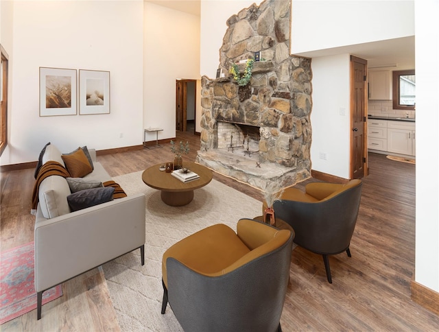 living area featuring a stone fireplace, baseboards, and wood finished floors