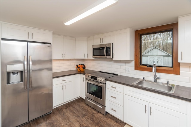 kitchen with dark countertops, appliances with stainless steel finishes, a sink, and white cabinetry