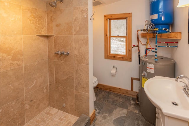 full bath featuring a tile shower, stone finish floor, toilet, vanity, and baseboards