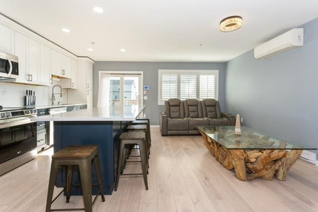 243 Sportsmans Ave, Freeport, NY 11520 - kitchen with white cabinets, stainless steel appliances, light wood finished floors, a kitchen bar, and a wall mounted air conditioner