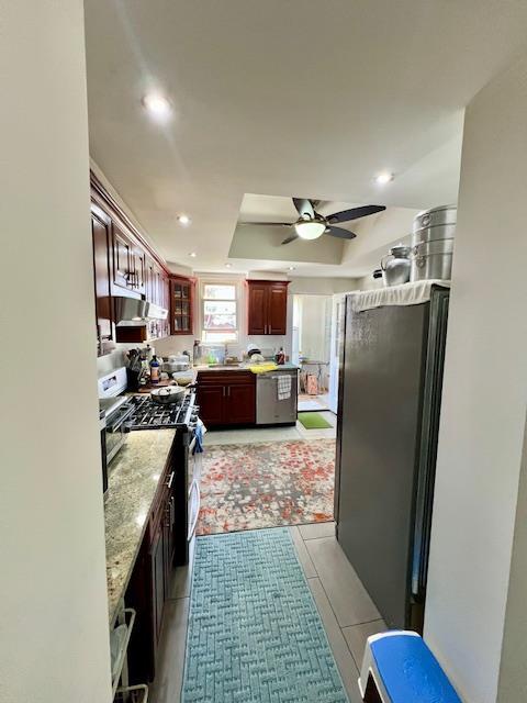 kitchen with ceiling fan, stainless steel appliances, a tray ceiling, light stone countertops, and recessed lighting